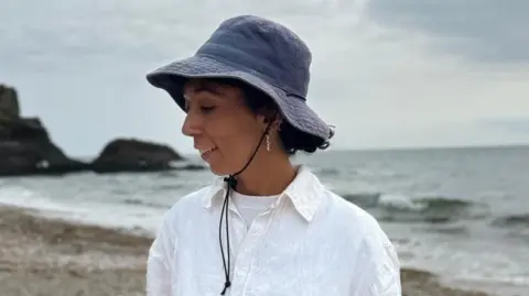 Tilly Kaye A woman with brown curly hair wearing a dark blue cap and a white shirt. 